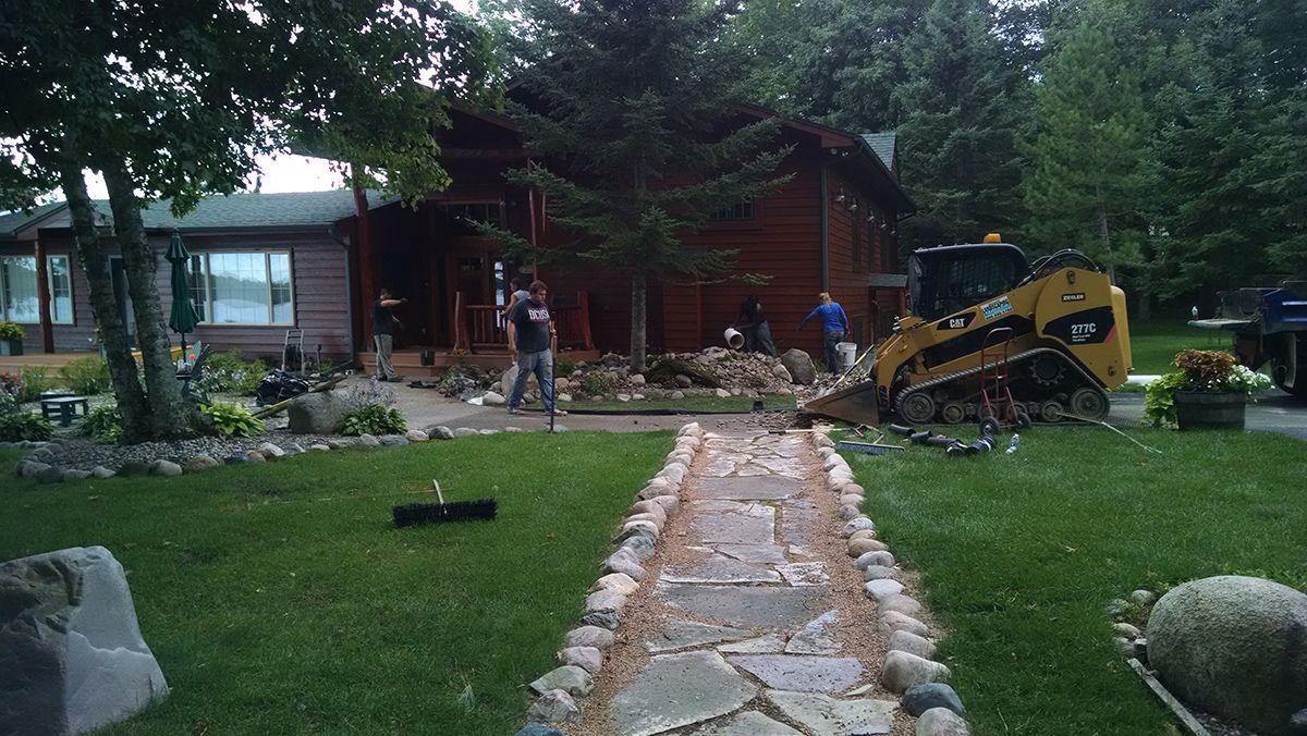 Yellow skid steer clearing debris beside a stone path in front of a house