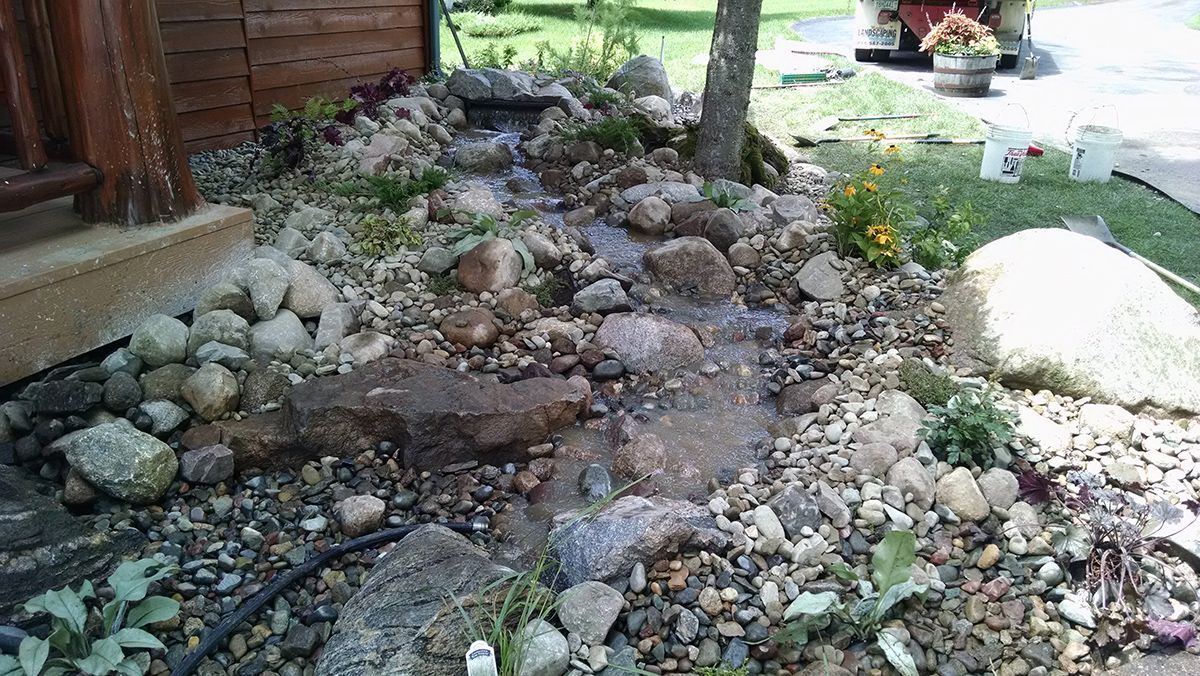 Rock garden beside a wooden house, with stones, gravel, and a tree in the center
