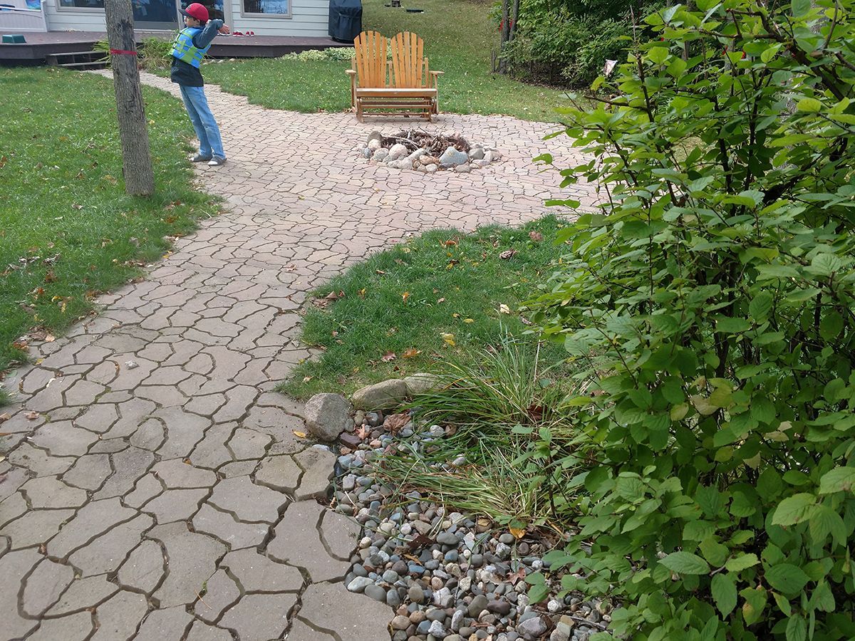 Person walking on a cracked garden path past a bench and greenery