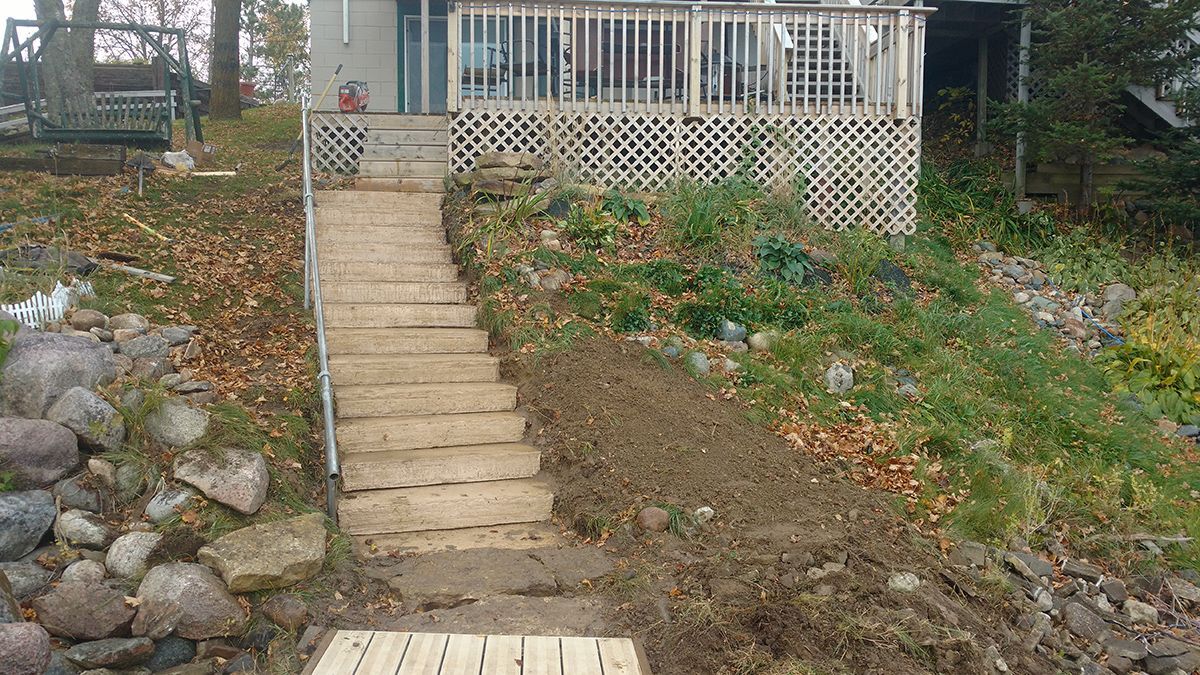 Front yard walkway with stone steps leading up to a porch, beside a rocky slope and patchy grass.