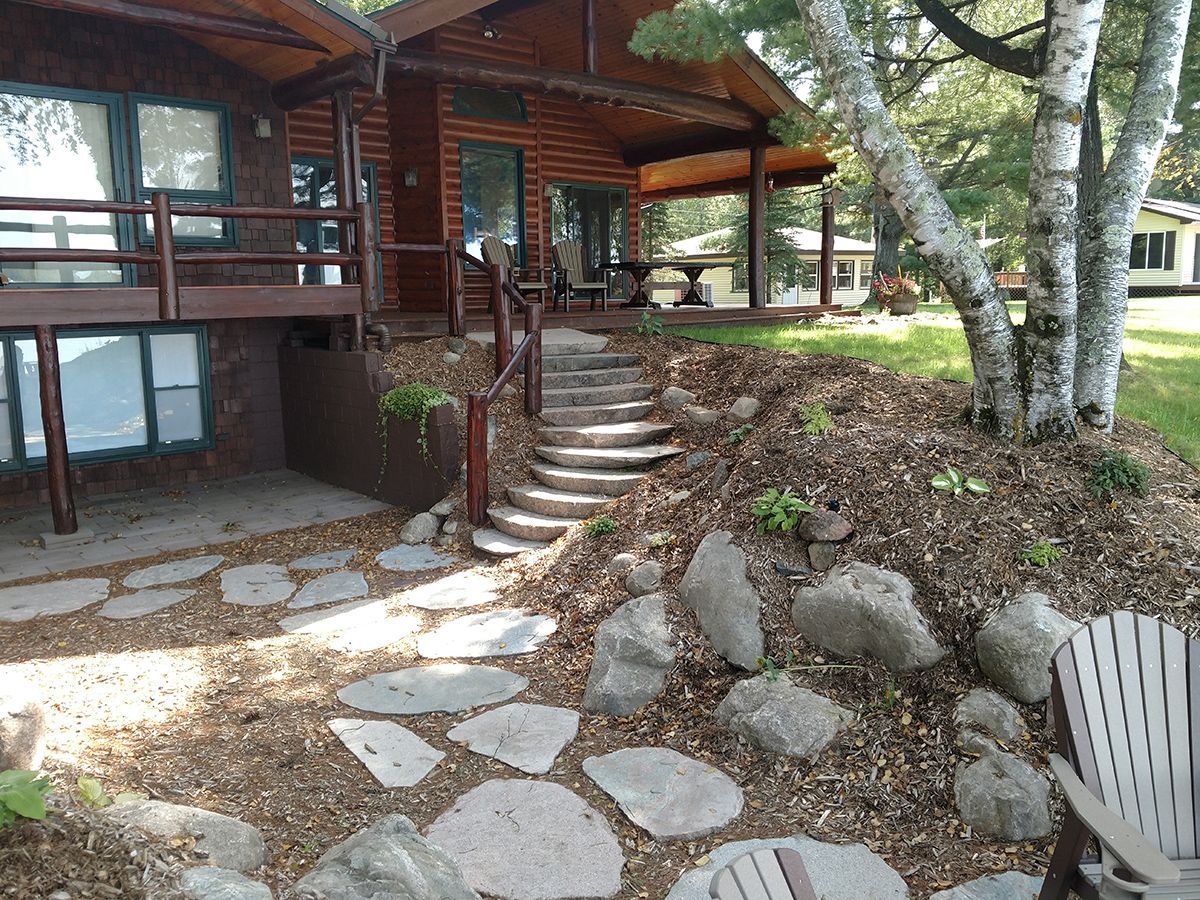 Wooden cabin with stone steps, rock path, and birch trees in a wooded yard