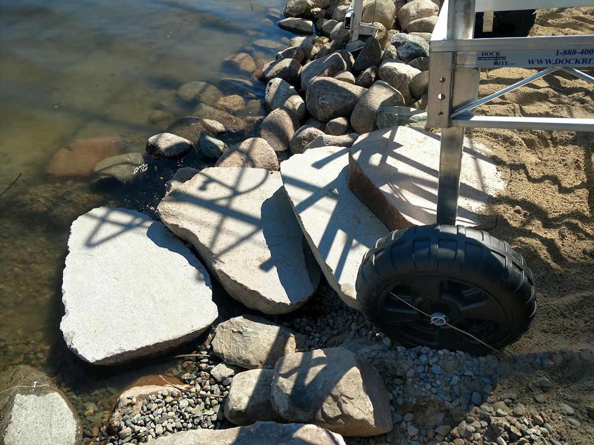 Shoreline path with white stepping stones, rocks, and a black tire border beside the water