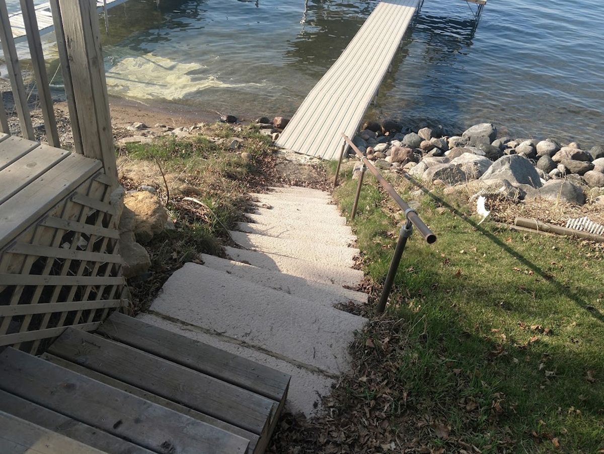 Steep concrete steps lead down to a narrow dock on a rocky shoreline beside calm water.