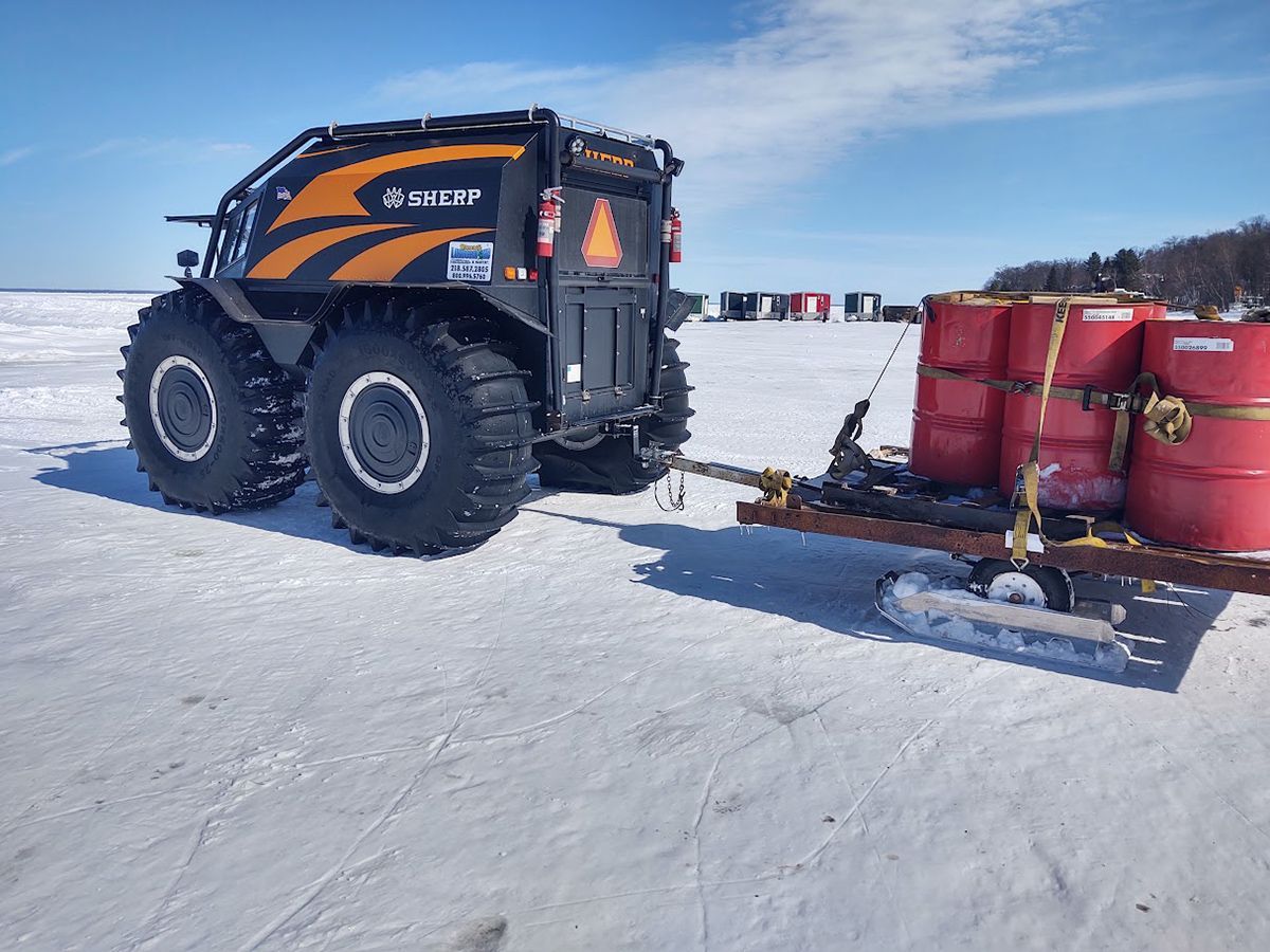 Orange snow tractor pulling red barrels across a snowy field