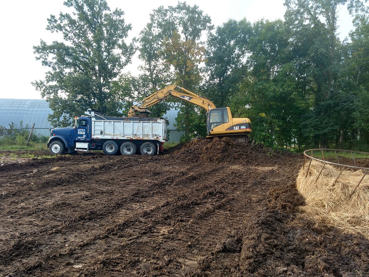 Excavator loading soil into a dump truck on a muddy construction site near trees