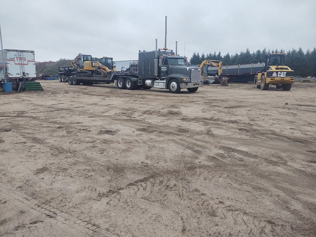 Heavy truck and machinery parked on a muddy construction site under an overcast sky