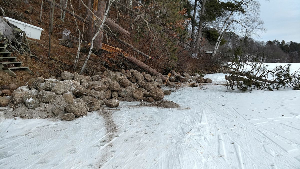 Snow-covered shoreline with rock outcroppings and bare trees along a winter path