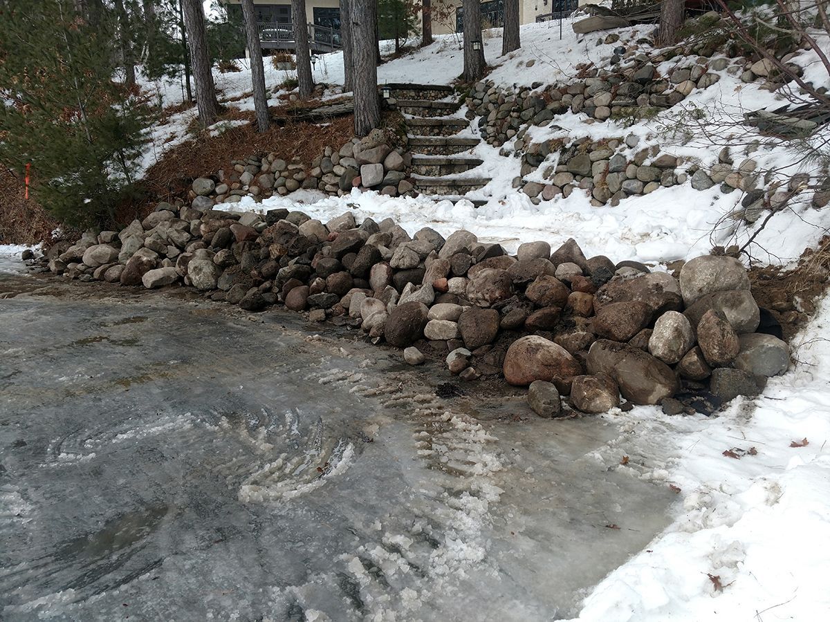 Snowy roadside with a stone retaining wall and steps beside a wet, icy surface
