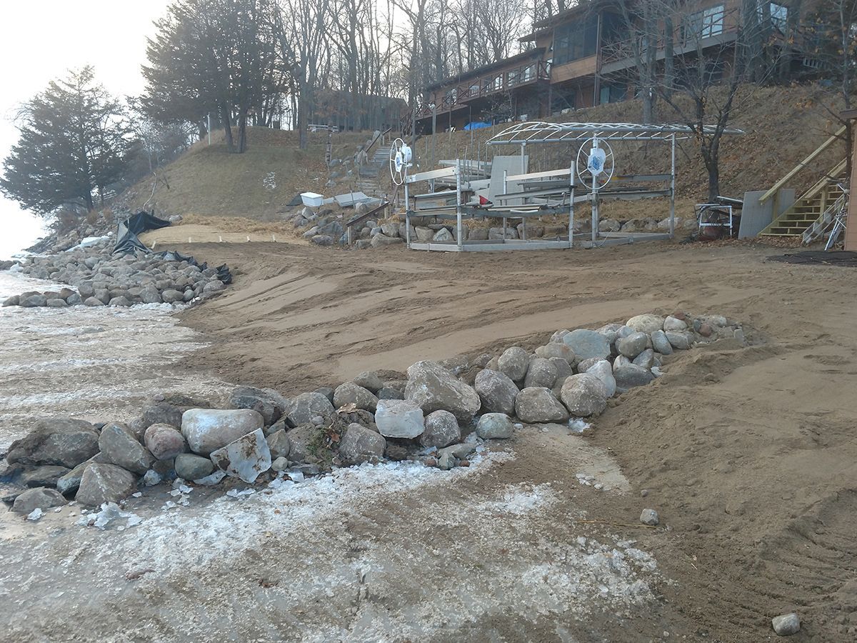 Rocky shoreline with ice, a sandy beach, and a raised deck beside leafless trees