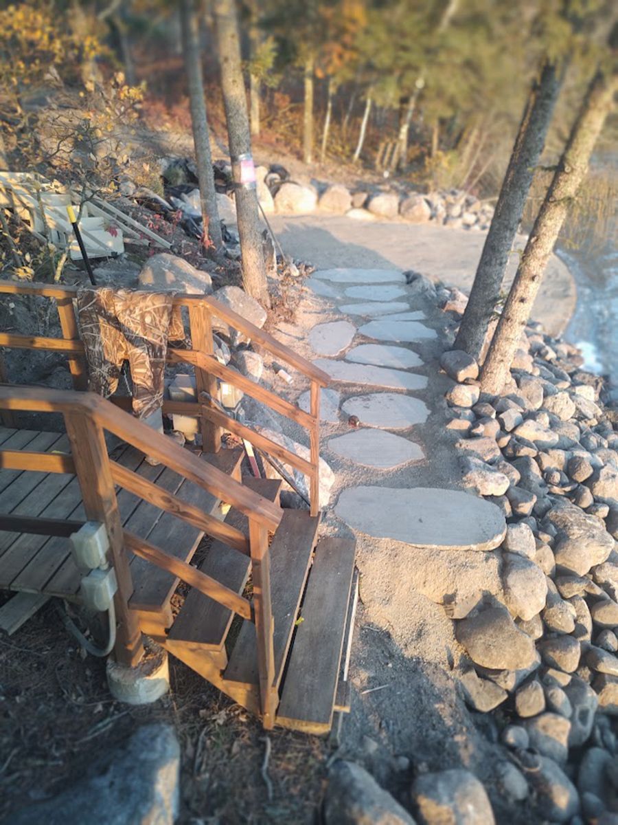 Stone path with wooden railing and steps through a rocky, tree-lined outdoor area