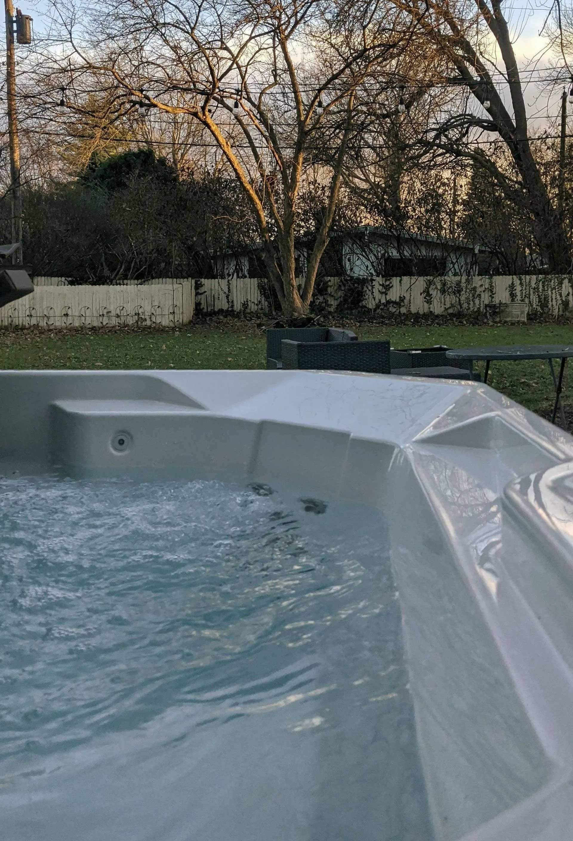 Hot tub with bubbling water, set outdoors near a fence and trees.
