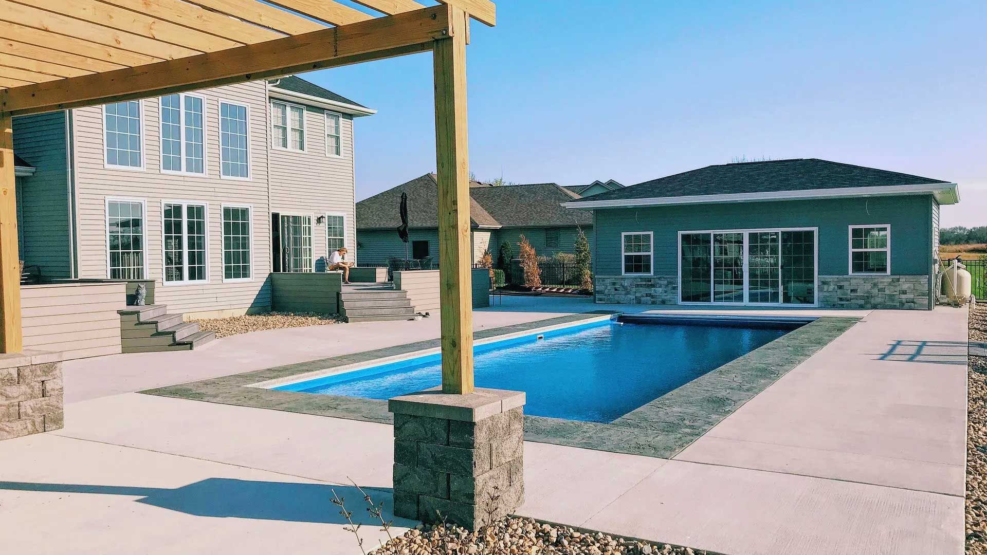 Backyard with a rectangular pool, house, and pergola under a blue sky.