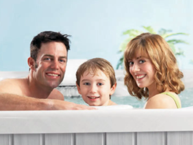 Family smiling together in a hot tub; blue sky and palm trees in the background.