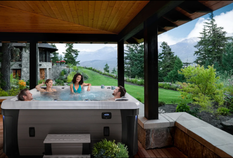 Four people relaxing in a hot tub on a deck with a mountain view.
