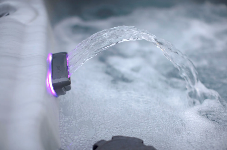 Close-up of a hot tub jet spraying water with a purple light illuminating it.