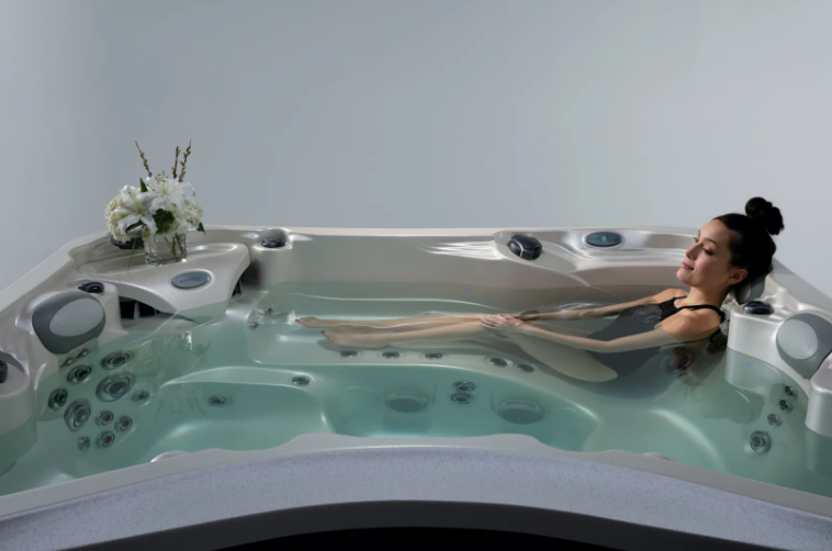 Woman relaxing in a hot tub, eyes closed, with a bouquet of flowers nearby, indoors.