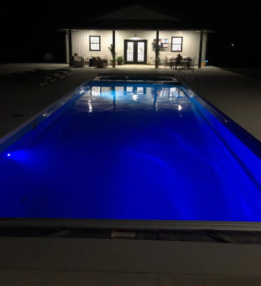 A rectangular pool with blue lights reflects a house at night.