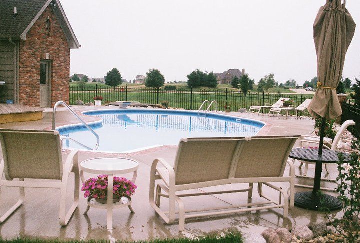 Backyard with a swimming pool, lounge furniture, and a partially open umbrella; overcast sky.
