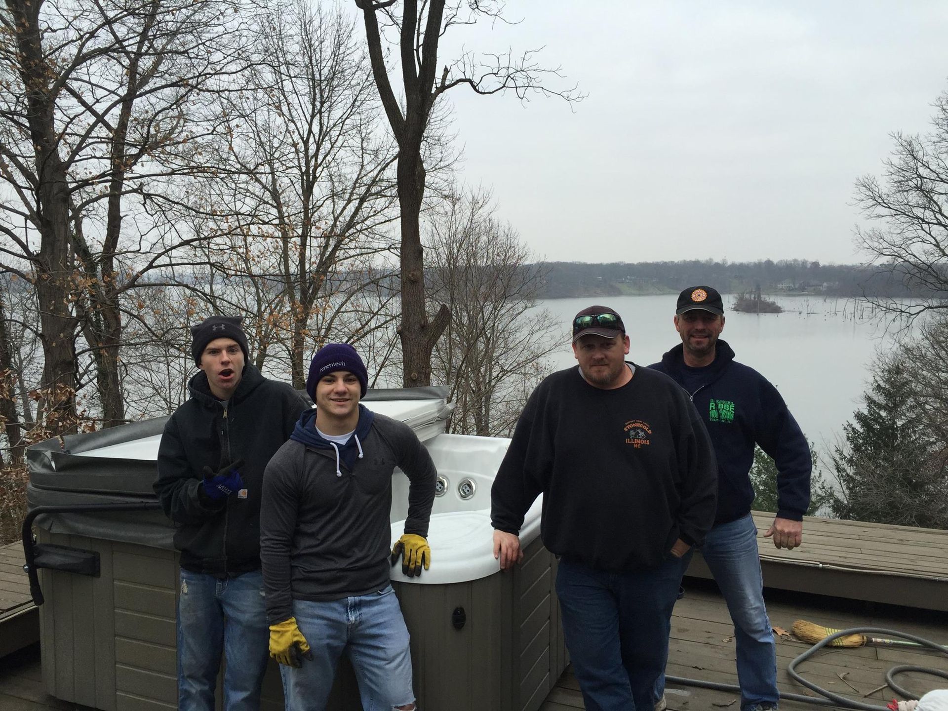 Four men near a hot tub overlooking a lake on a cloudy day.