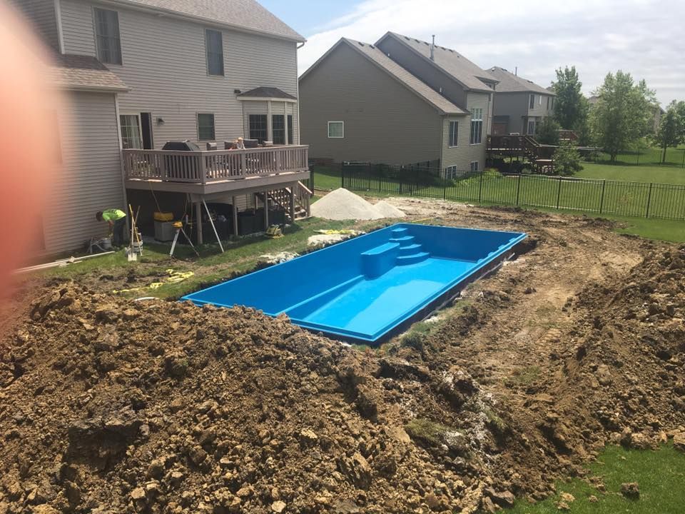 New blue swimming pool under construction in a backyard, surrounded by dirt and houses.