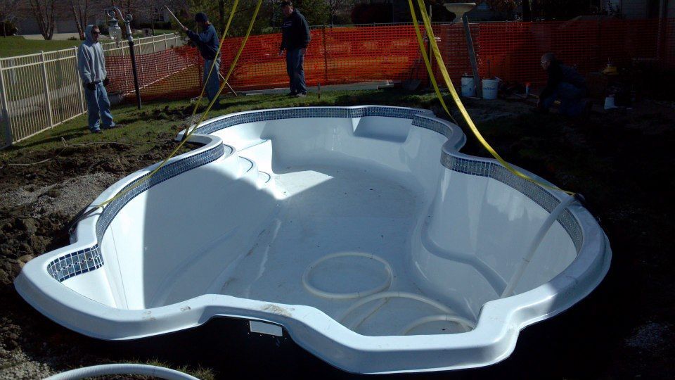 Pool being installed in a yard, with workers nearby.