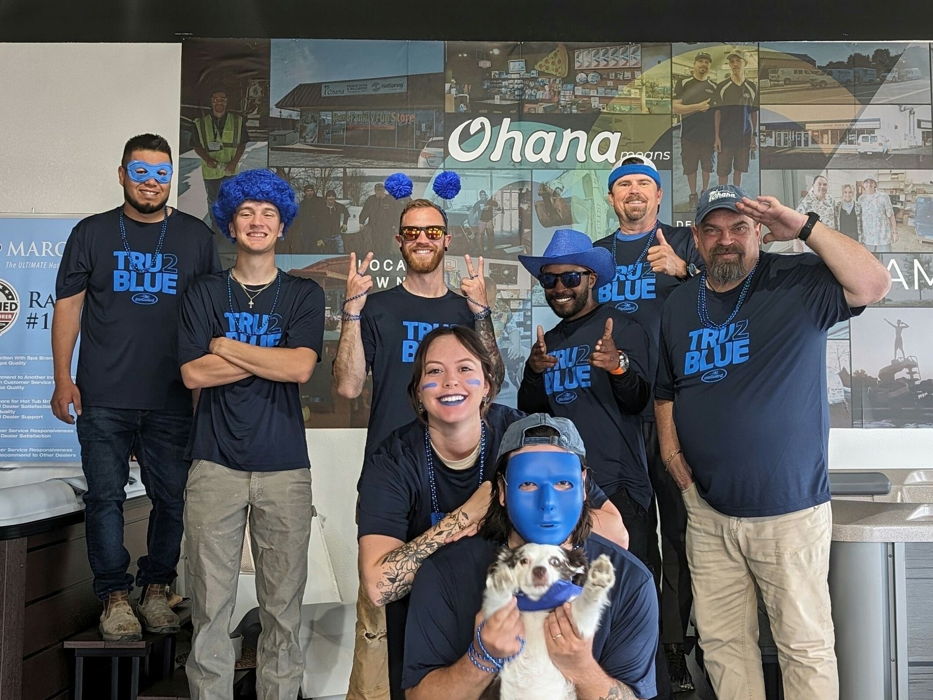 Group of people in blue shirts and costumes posing, in front of a 