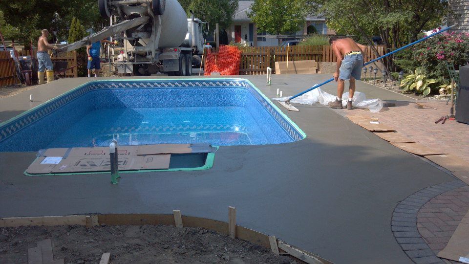 Concrete being poured around a rectangular swimming pool, workers smoothing the wet concrete.