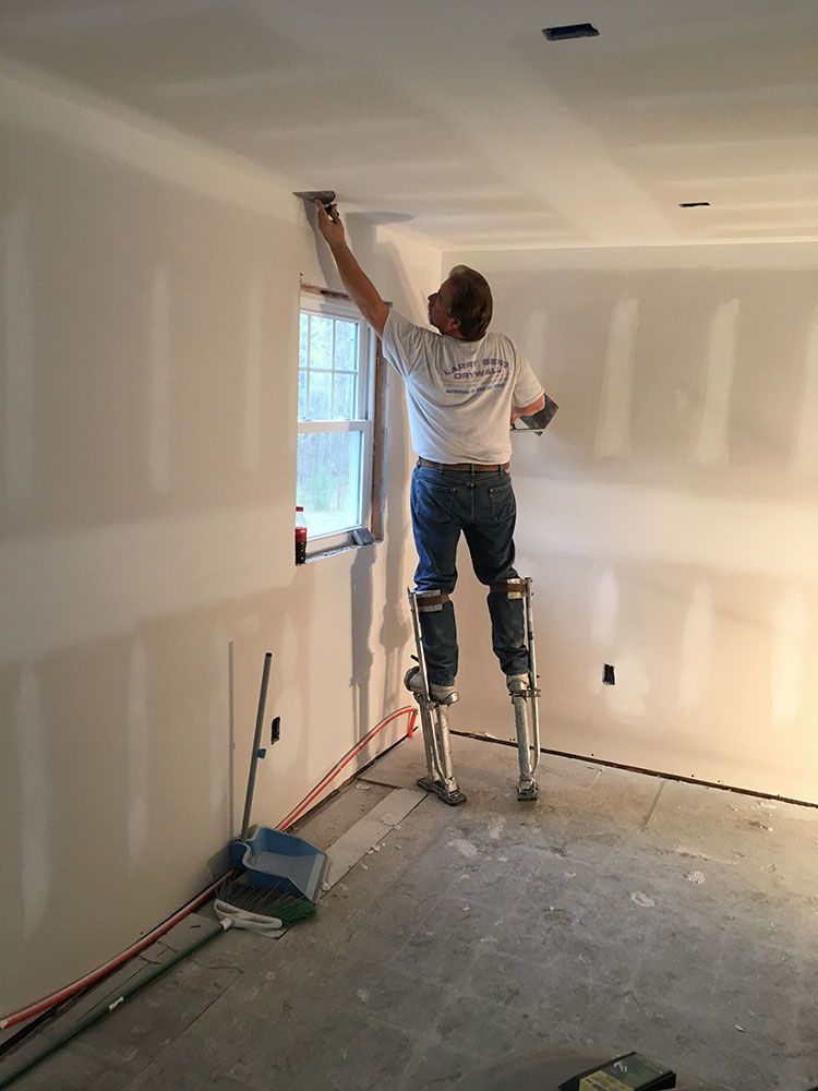 A man is standing on stilts painting a wall.