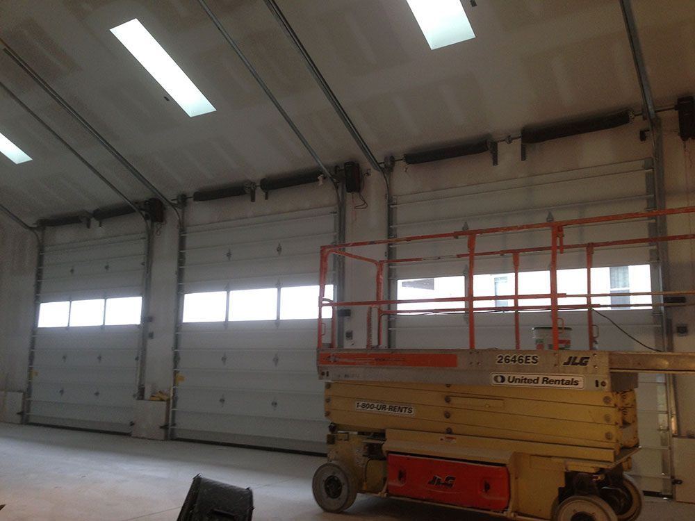 A scissor lift is parked in front of a large garage door.