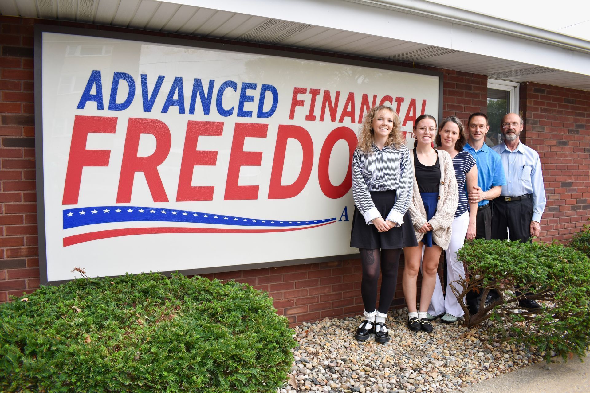 Four people standing outside an office beside a sign reading Advanced Financial Freedom