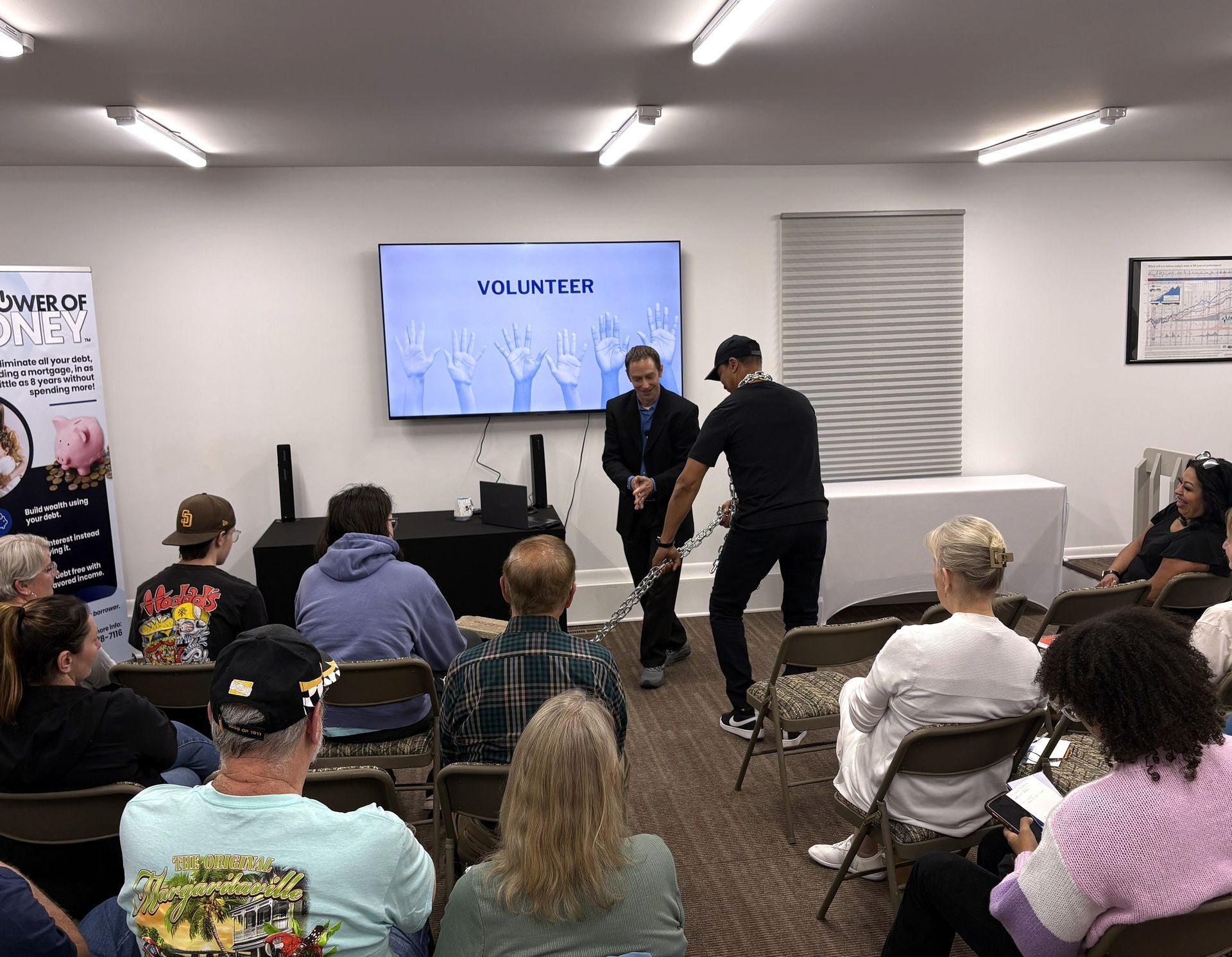 Audience seated in a meeting room watching two presenters beside a screen displaying VICTORIES