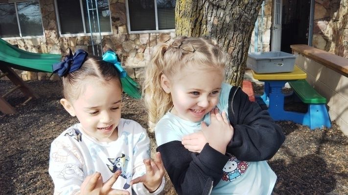 Two little girls are standing next to each other in a playground.