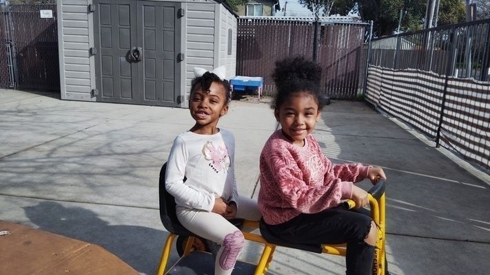 Two little girls are sitting on a yellow bicycle.