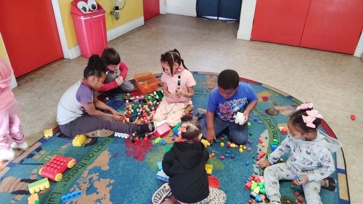 A group of children are sitting on the floor playing with lego blocks.