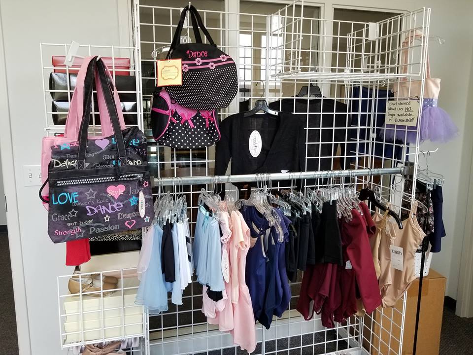 A retail display with dance clothing, accessories, and bags. Clothing is hanging on a rack, while bags and a tutu dress are hung above.