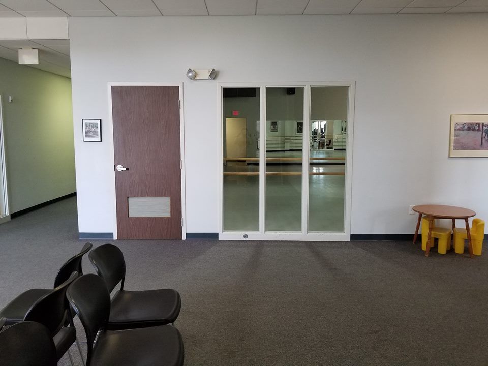 Awaiting area with chairs, a door, mirrors, and a small table with yellow stools.