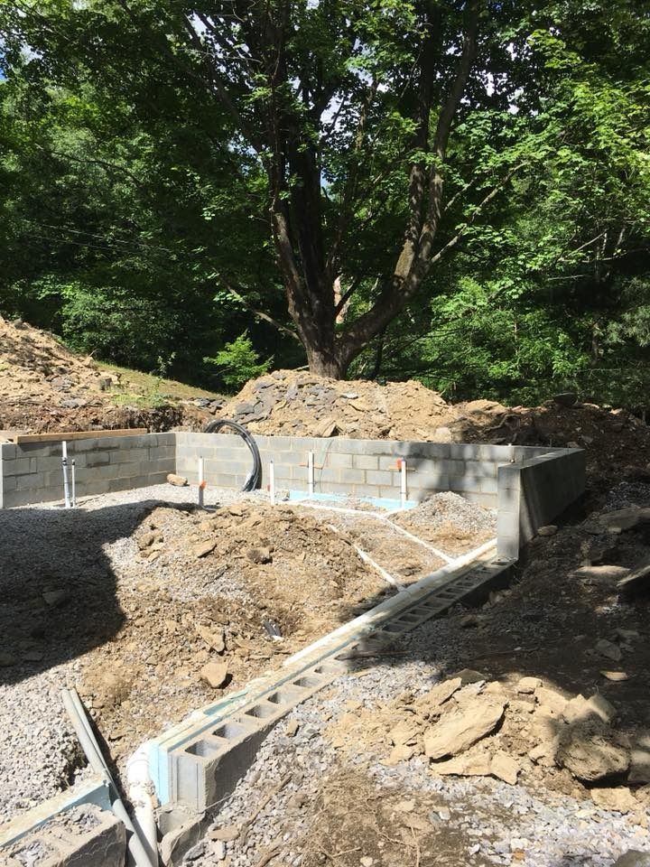 Foundation of a building under construction, next to a large tree, on a hillside.