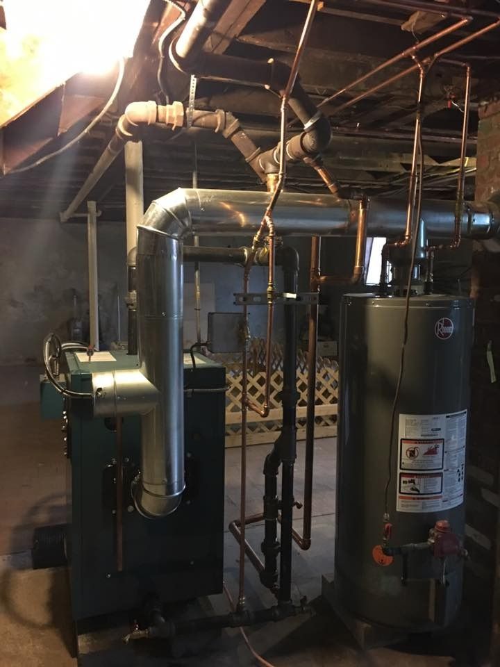 Furnace and water heater in a basement. Silver metal vents and copper pipes.
