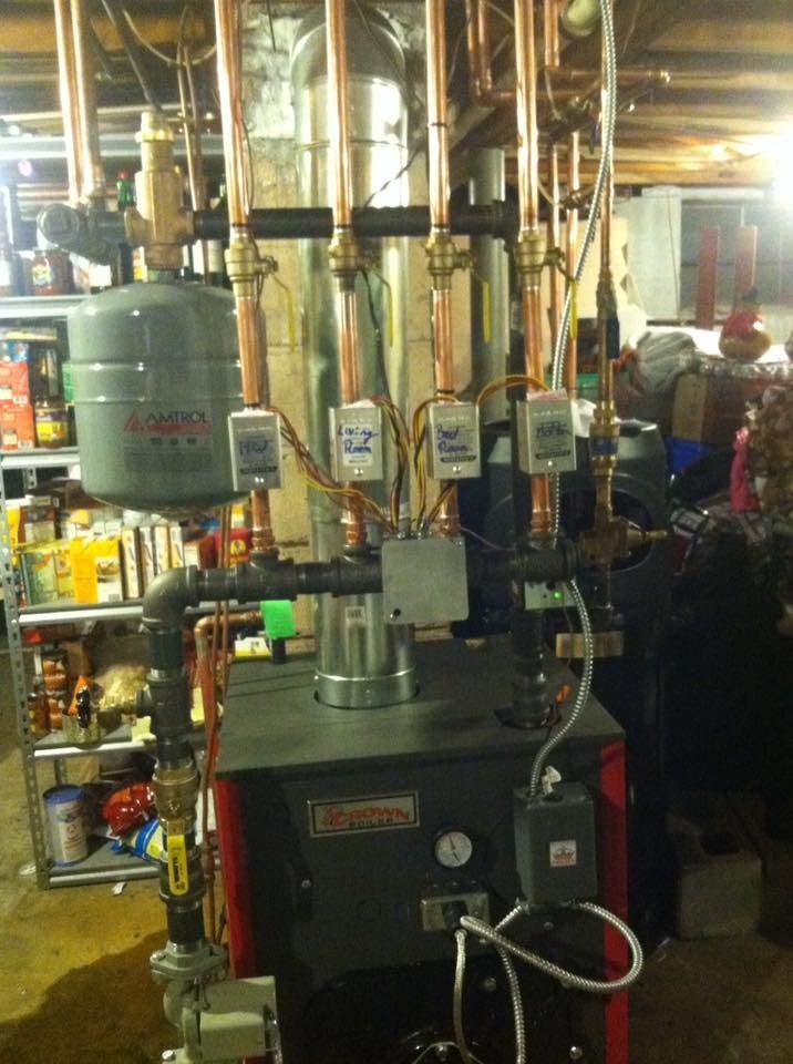 A residential boiler system with copper pipes, expansion tank, and control boxes in a basement.