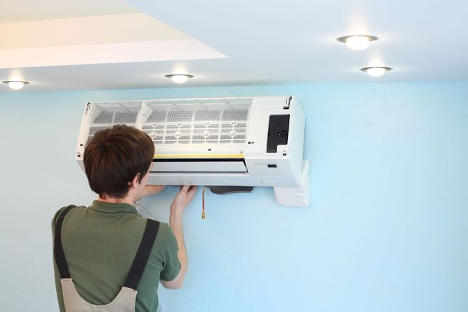 A technician installs an air conditioning unit on a light blue wall.