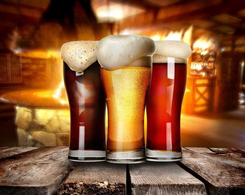 Three glasses of beer are sitting on a wooden table.