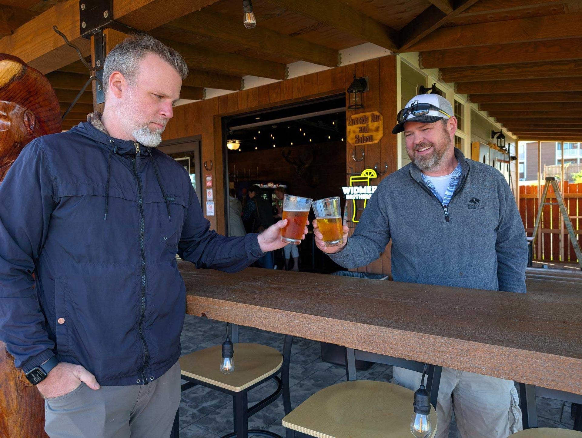 Two men are standing at a bar holding glasses of beer.