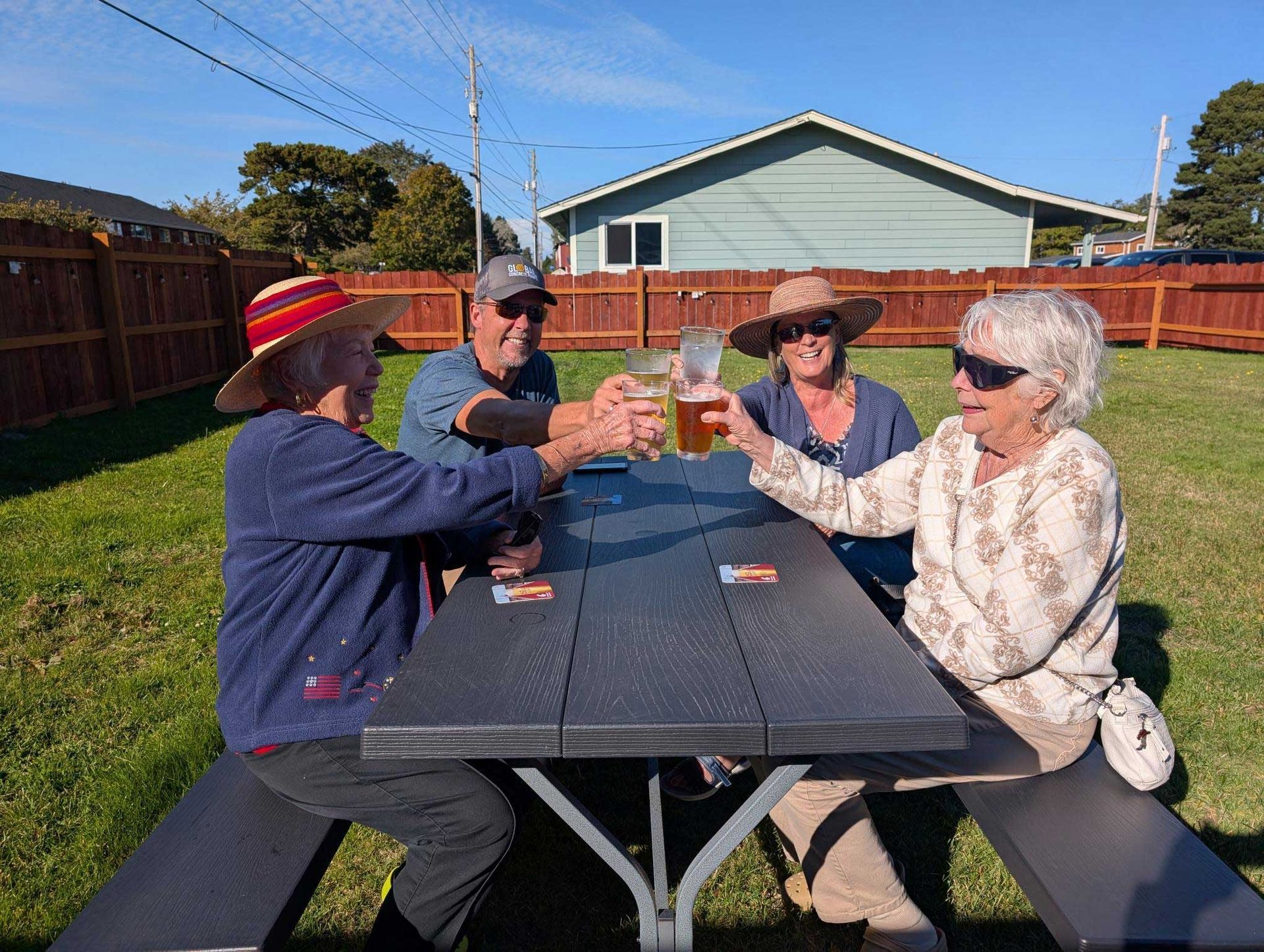 A group of people are sitting at a picnic table toasting with beer.