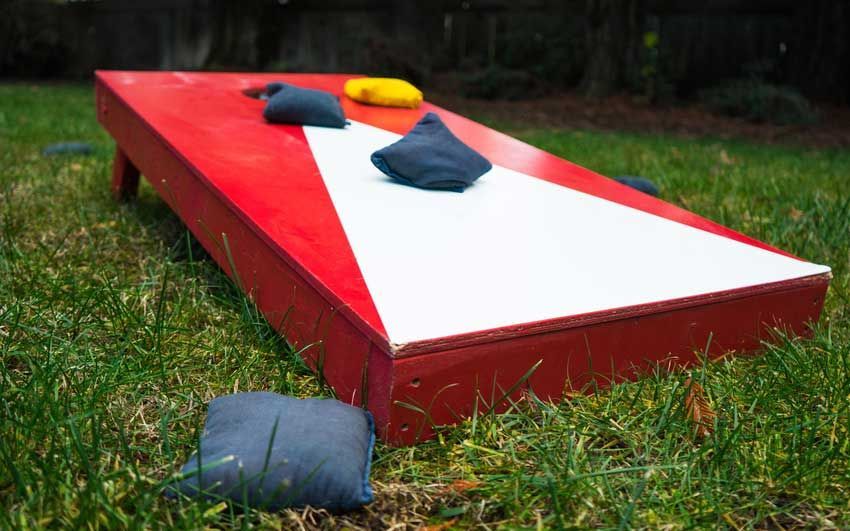 A red and white cornhole board is sitting on top of a lush green field.
