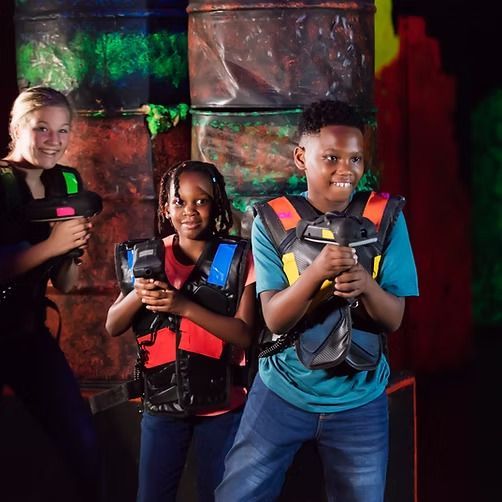 A boy and two girls are playing laser tag in a dark room.