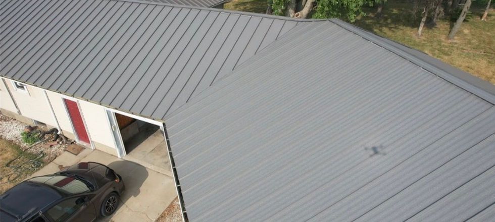 A car is parked in front of a house with a gray roof.