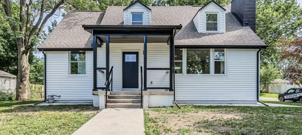 A white house with a black door and porch is for sale.