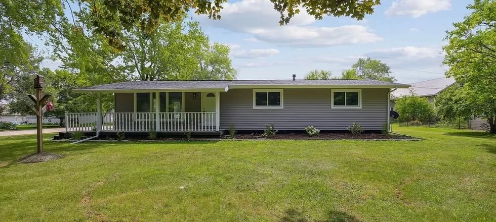 A house with a porch and a large lawn in front of it.