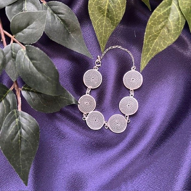 A silver bracelet is sitting on a purple cloth