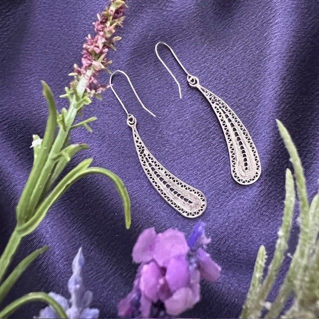 A pair of earrings are sitting on a purple cloth next to purple flowers
